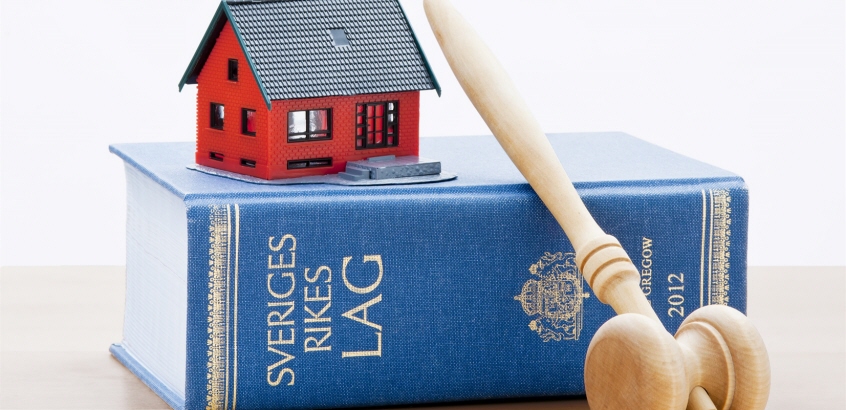 Ett litet tecknat rött hus ovanpå en lagbok, en domarklubba i trä som ligger lutad mot lagboken.